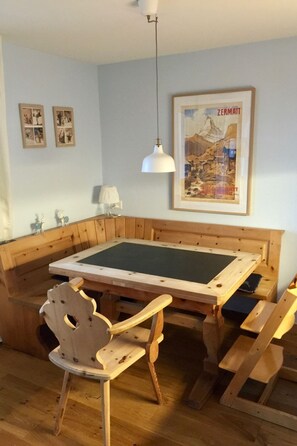 Ein Zimmer mit einer hölzernen Bank und einem Tisch, einem gerahmten Bild an der Wand und einer Pendelleuchte.