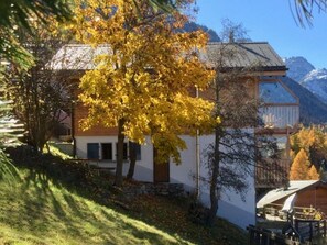 A building with a sloped roof, a stone foundation, and a view of mountains in the background. - Anita, (Grächen), 1055 by Interhome (Grächen)