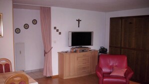 A living room with a television, a wooden cabinet, a red leather chair, a wooden wardrobe, and a wall with a cross and clocks. - Castello, (Grächen), 1322 by Interhome (Grächen)