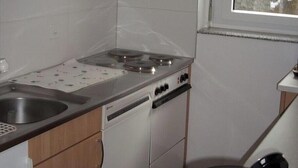 A compact kitchen with wooden cabinets, a stove, a sink, and a window with a view. - Castello, (Grächen), 1322 by Interhome (Grächen)