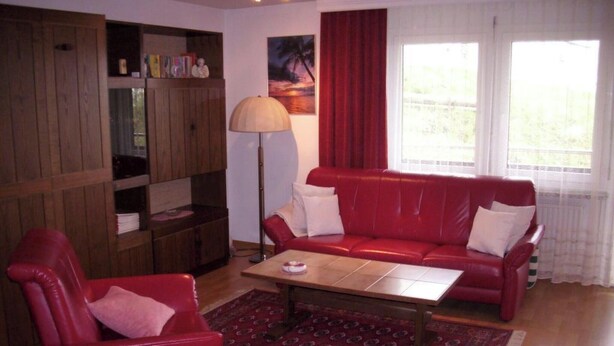 A living room with a red sofa, a wooden cabinet, a floor lamp, and a window with curtains. - Castello, (Grächen), 1322 by Interhome (Grächen)