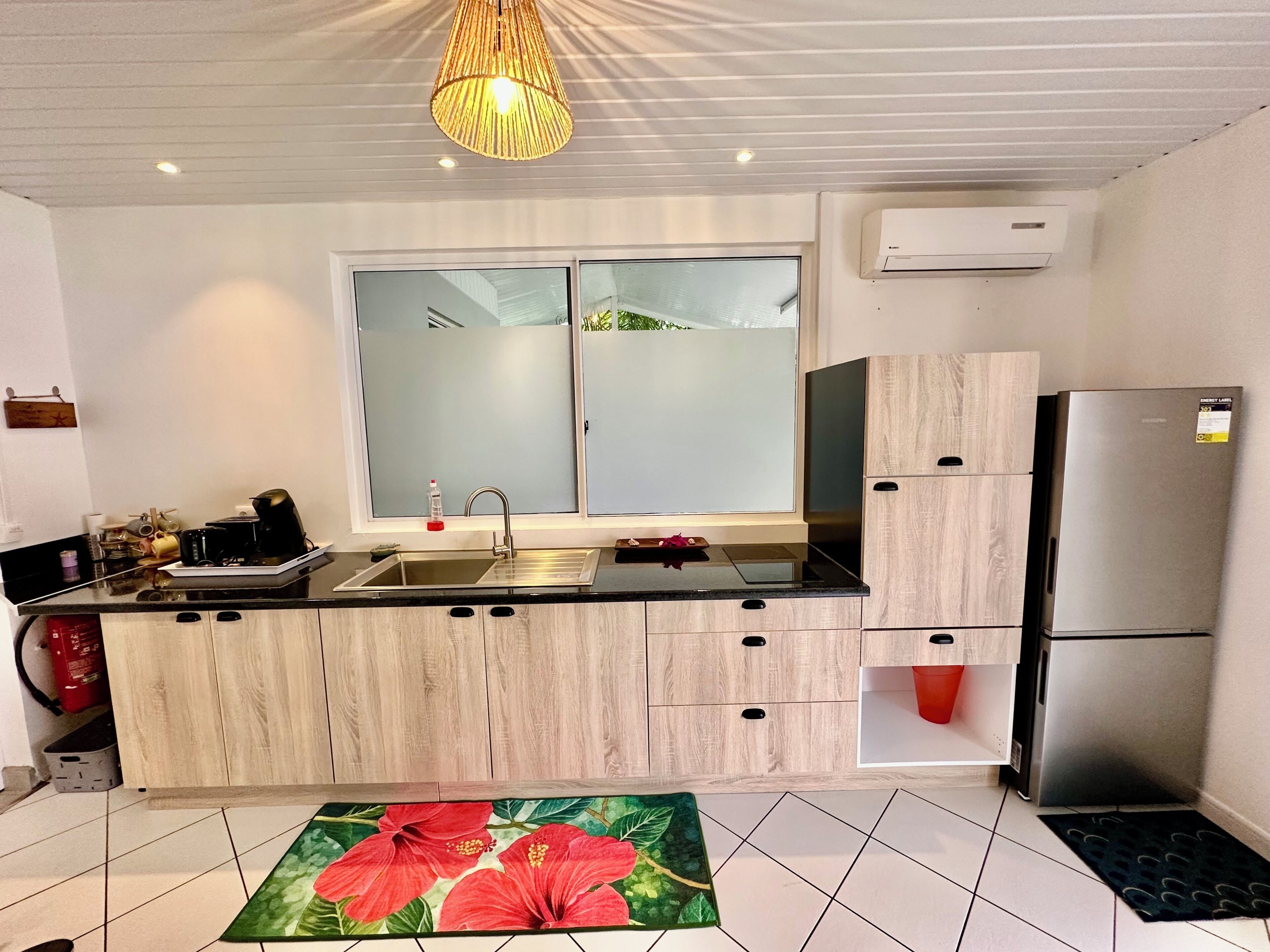 A modern kitchen with a black countertop, wooden cabinets, a stainless steel sink, and a refrigerator.