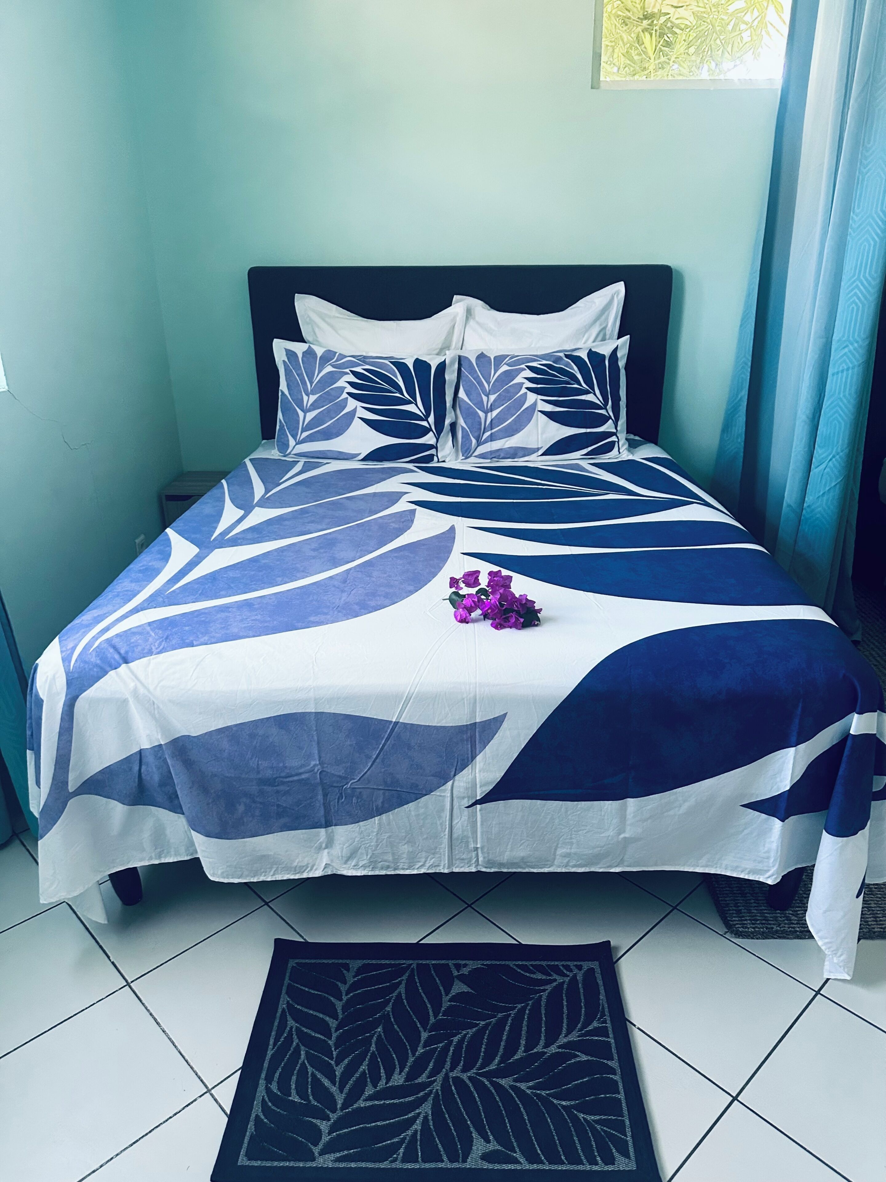 A bed with a leaf-patterned bedspread, a pillow, and a small bouquet of flowers.