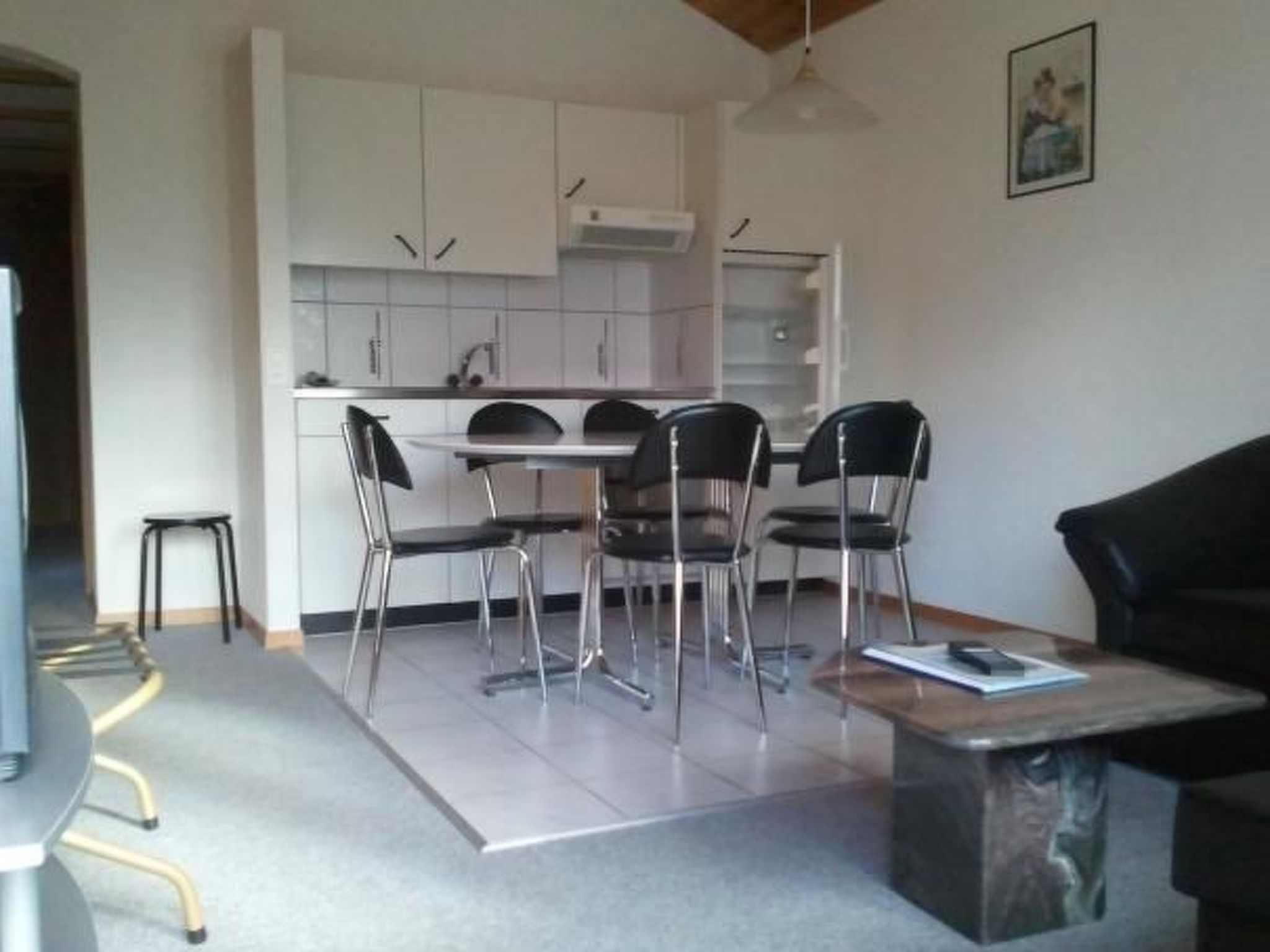 A modern kitchen with white cabinets, a dining table with four chairs, and a small stool.
