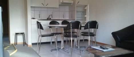 A modern kitchen with white cabinets, a dining table with four chairs, and a small stool.