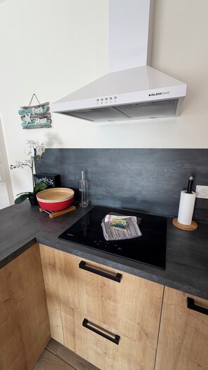 A kitchen with a black countertop, wooden cabinets, a white range hood, and a black induction cooktop. - BEACH HOUSE, Vensac Océan, just outside Montalivet: a cozy little getaway for two! (Vensac)