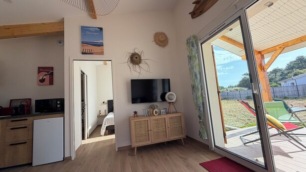 Ein Zimmer mit Holzboden, einem an der Wand montierten Fernseher, einer Kommode mit einem dekorativen Gegenstand und einer Glastür, die zu einem Außenbereich führt.