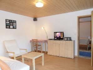 Ein Wohnzimmer mit Fernseher, einem Sessel, einem Tisch und einem Schrank.