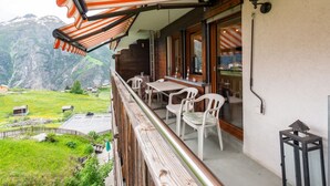 Een balkon met uitzicht op een bergachtig landschap, een tafel met stoelen en een houten hekwerk.