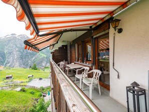 Ein Balkon mit Blick auf eine gebirgige Landschaft, ein Tisch mit Stühlen und ein Holgitter.