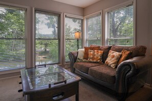 Ein Zimmer mit Ledersofa, einem Glastisch und großen Fenstern mit Jalousien.