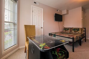 A room with a bed, a table with a game, a chair, a television, and a window with blinds. - Riverfront home near Dollywood and Pigeon Forge Parkway! (PIGEON FORGE)