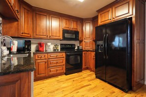 A kitchen with wooden cabinets, a black refrigerator, a microwave, a coffee maker, and a stove. - Riverfront home near Dollywood and Pigeon Forge Parkway! (PIGEON FORGE)