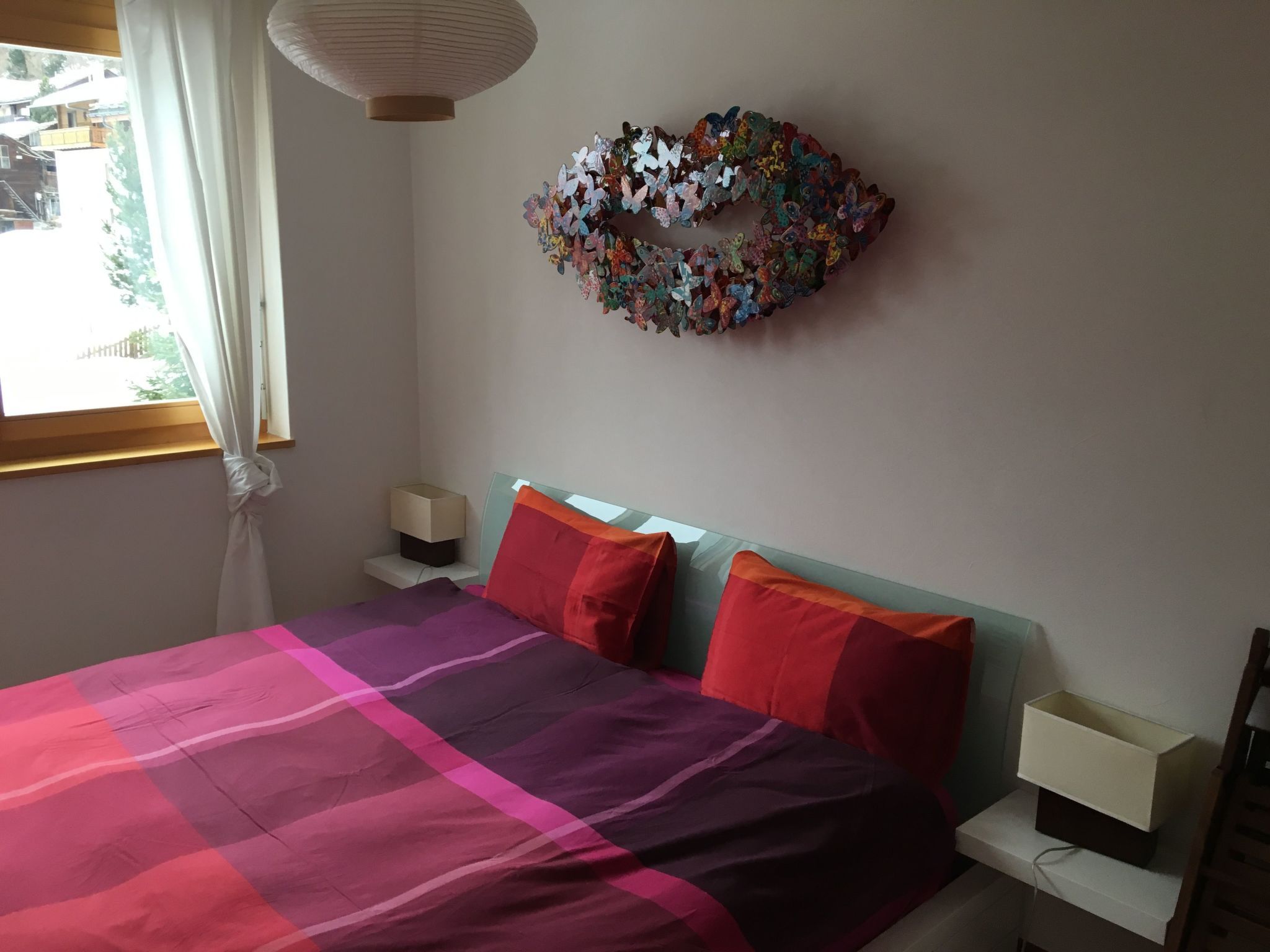 A bedroom with a bed, pillows, a nightstand, a wall-mounted lamp, and a butterfly wall art piece.