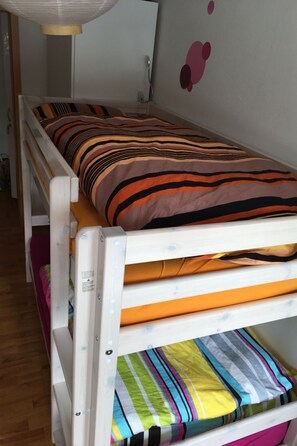 Ein Stockbett mit gestreifter Bettwäsche, eine weiße Wand mit einem rosa abstrakten Design und ein Holzboden.