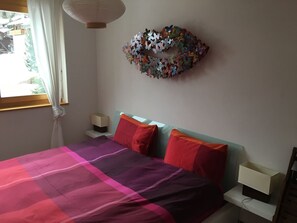 Ein Schlafzimmer mit Bett, Kissen, Nachttisch, Wanddeko und einem Fenster mit Vorhängen.