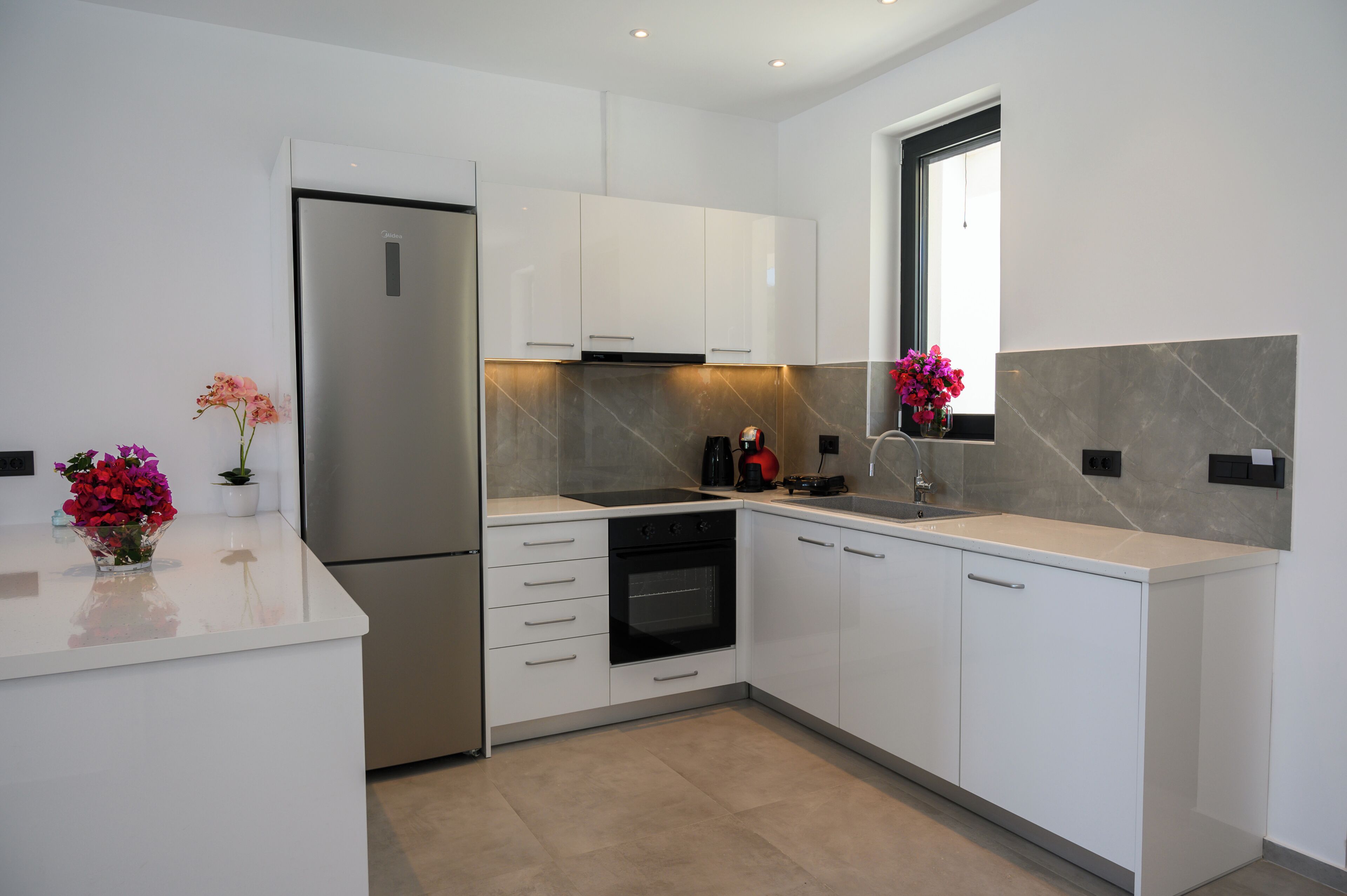 A modern kitchen with white cabinetry, a stainless steel refrigerator, an oven, and a window with a view.