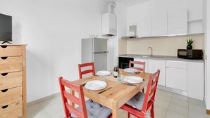 A modern kitchen with white cabinets, a wooden dining table with four chairs, and a microwave on the counter. - CO14 [Central] • Comfort • (Milano)