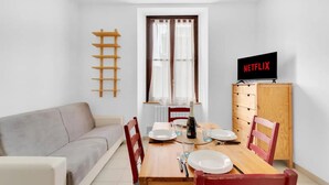 A compact living space with a dining table, chairs, a sofa, a TV, and a wooden cabinet. - CO14 [Central] • Comfort • (Milano)