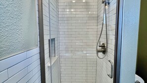Eine gläserne Duschkabine mit weißen Fliesen im U-Bahn-Stil, einer Handbrause und einem Ablauf.