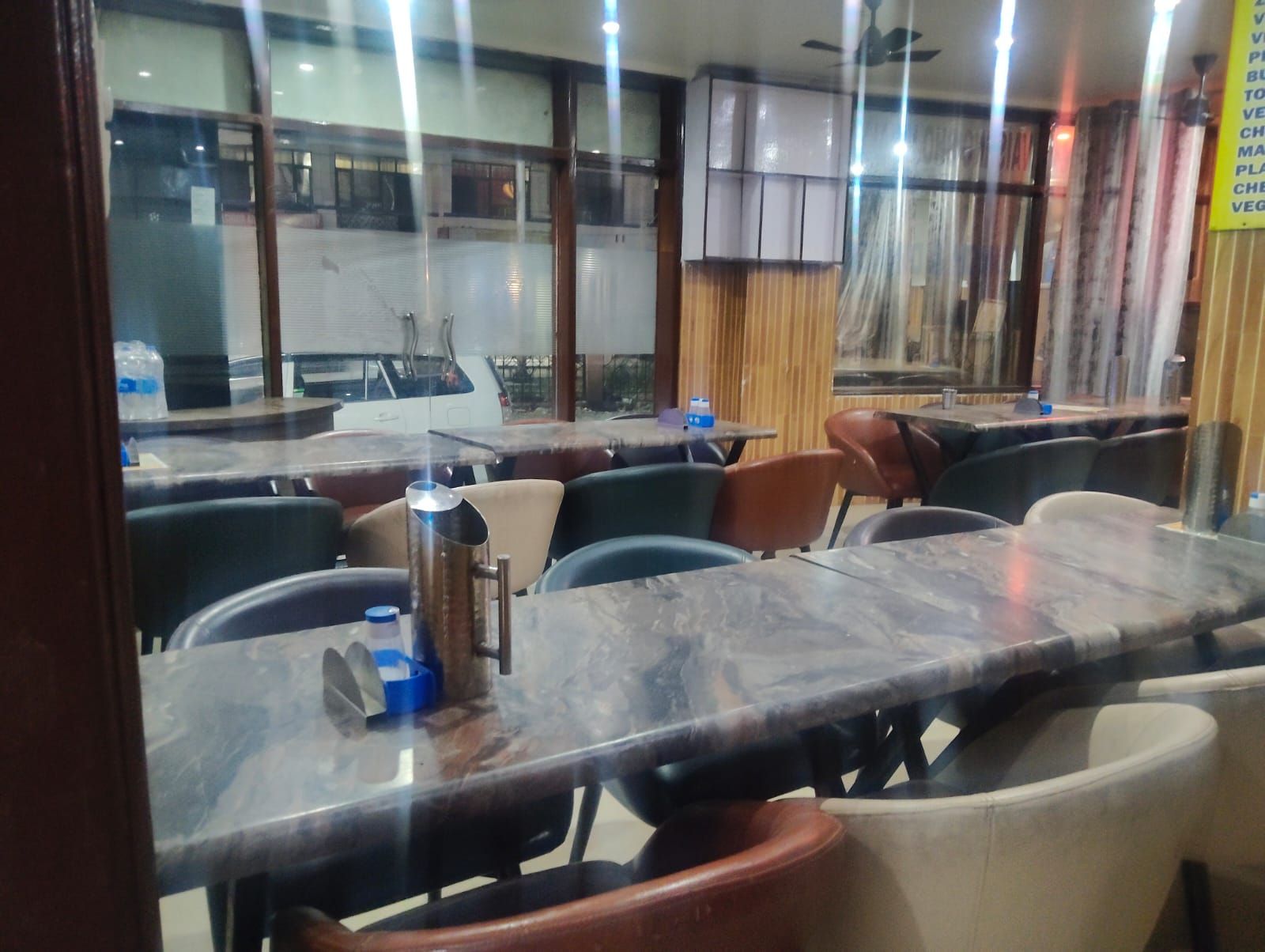 Un interior de restaurante con mesas, sillas, dispensador de agua y vista al exterior.