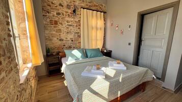 Un dormitorio con pared de piedra, una cama con colcha estampada, una mesita de noche, una lámpara y una puerta.