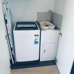 A compact laundry room with a washing machine, a small sink, and a basket. - Great views - Apartment in Canberra CBD (Reid)