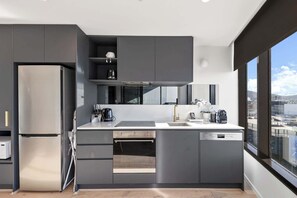 A modern kitchen with a built-in oven, a dishwasher, and a large window offering a city view. - Great views - Apartment in Canberra CBD (Reid)