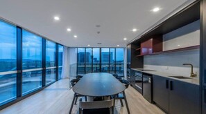 A modern kitchen with a large island, a dining area with a round table, and large windows offering a city view. - Stylish Apartment in Canberra CBD (Reid)