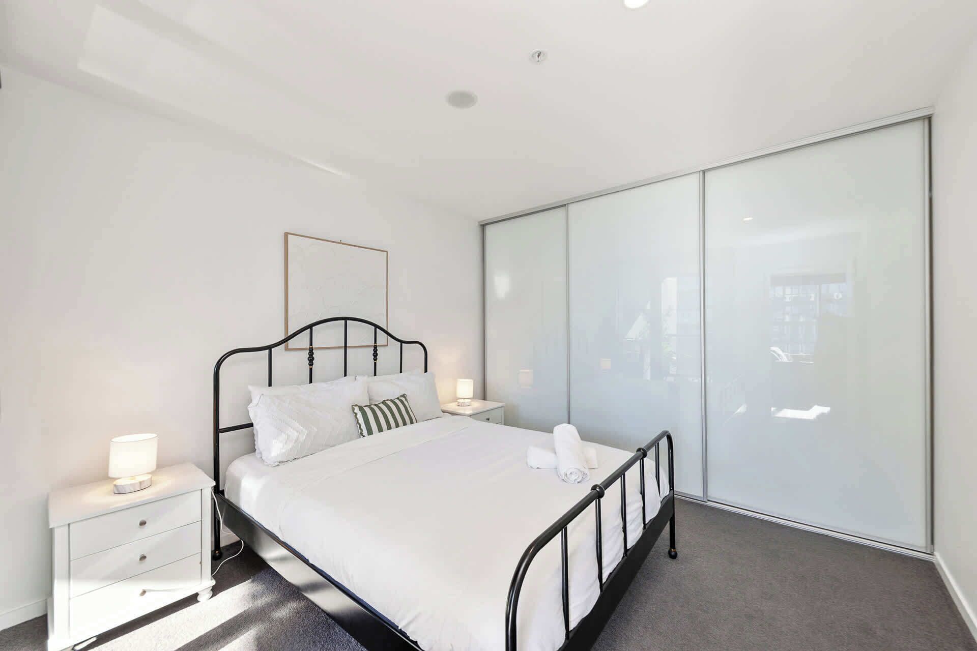 A modern bedroom with a bed, bedside tables, and a large wardrobe.