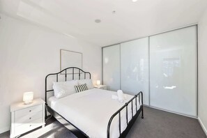 A modern bedroom with a bed, bedside tables, and a large wardrobe. - Great views - Apartment in Canberra CBD (Reid)