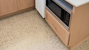 Een keuken met een wit aanrecht, houten kastjes, een roestvrijstalen oven en een raam met uitzicht op groen.