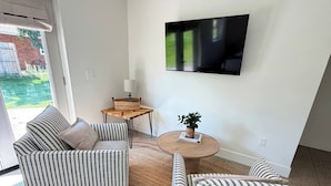 Een woonkamer met gestreepte banken, een flatscreen televisie aan de muur en een kleine ronde tafel met een lamp.