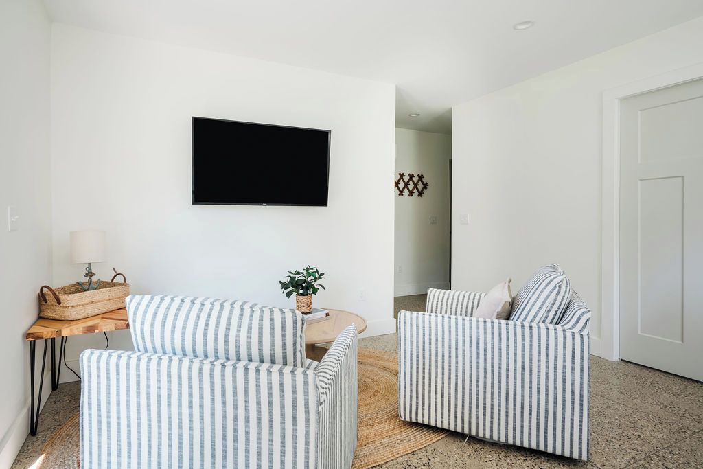 A living room with two striped sofas, a flat-screen TV, a small table with a lamp, and a woven basket.
