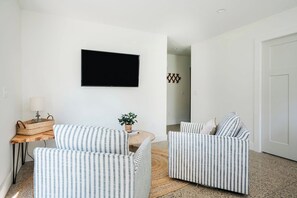 Un salon avec deux canapés à rayures, un téléviseur à écran plat, une petite table avec une lampe et un panier en osier.