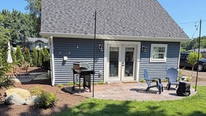 Een gelijkvloers huis met een overdekte patio, een barbecue en buitenmeubels.
