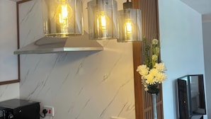 A kitchen with a stove, a wall-mounted light fixture with three bulbs, and a flower vase.