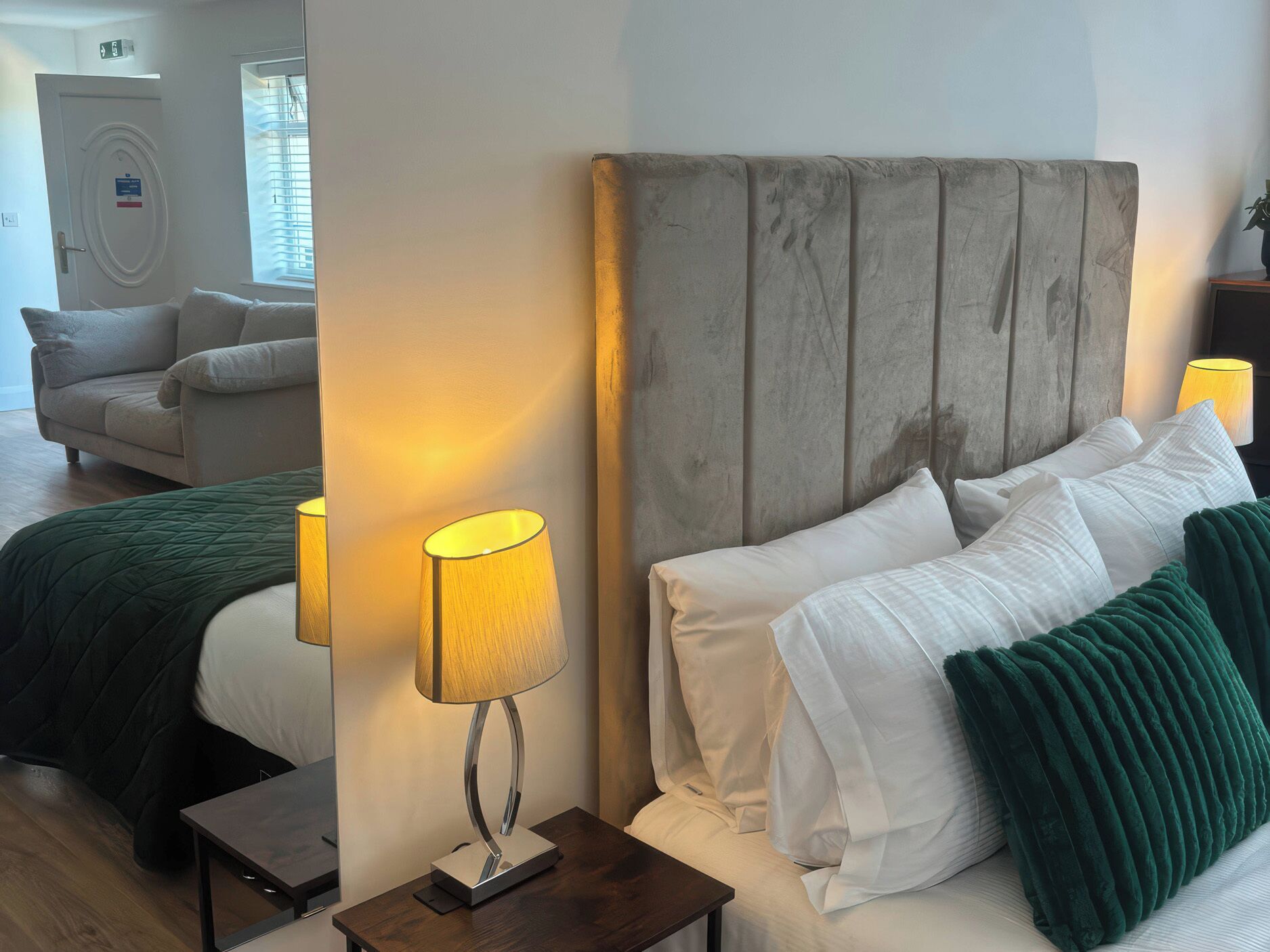 Quarto de hotel com cama, abajures, mesa de cabeceira e vista para o corredor.