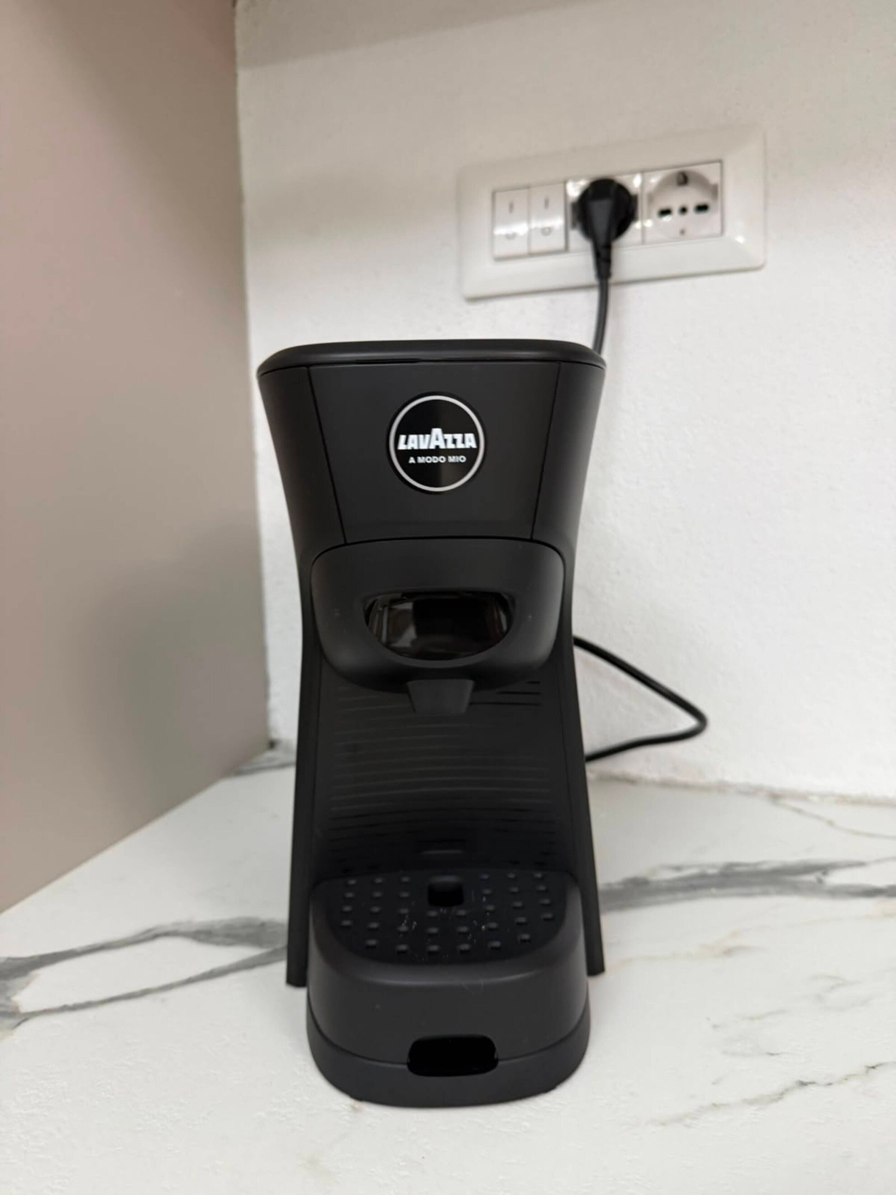 A black portable coffee machine with a plug, placed on a white surface.