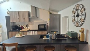Eine moderne Küche mit einer zentralen Kochinsel, Barhocker, einer großen Wanduhr und einem Kühlschrank.