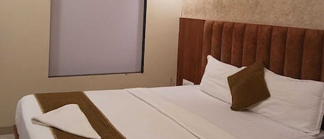 Habitación de hotel con cama, aire acondicionado de pared, lámpara colgante y ventana con persiana.