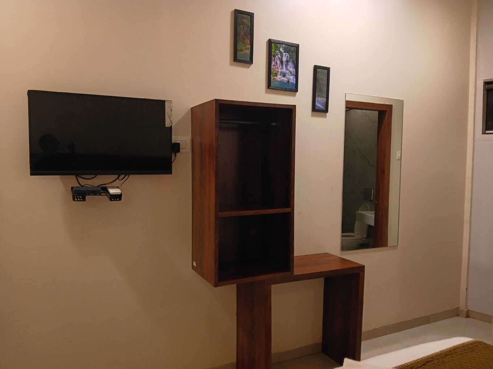 Une pièce dotée d’un téléviseur à écran plat fixé au mur, d’un meuble en bois et d’un miroir.