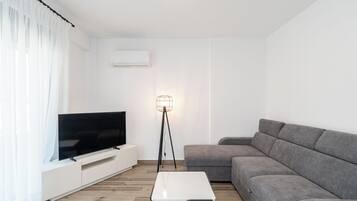 A modern living room with a flat-screen TV, a grey sofa, a white coffee table, and a floor lamp.