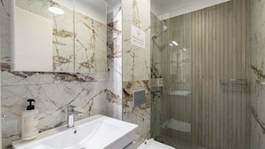 Een badkamer met een marmeren spatwand, een wit wastafelmeubel, een toilet en een douchecabine met glazen wanden.