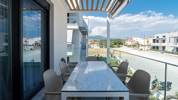 Een balkon met een tafel en stoelen, een pergola en uitzicht op de omliggende gebouwen.