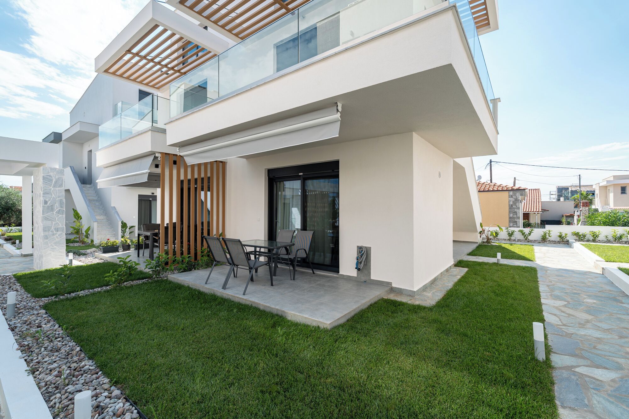 Una casa moderna de dos plantas con techo plano, un porche cubierto con mobiliario exterior y un césped bien cuidado.