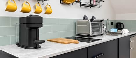 A modern kitchen with a coffee maker, toaster, and hanging yellow mugs.