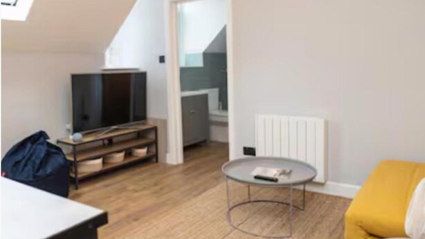 Een moderne woonkamer met een bank, een salontafel, een televisie op een dressoir en een trap naar een hoger niveau.