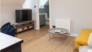 Uma sala de estar moderna com um sofá, uma mesa de centro, uma TV sobre um suporte e uma escada que leva a outro andar.