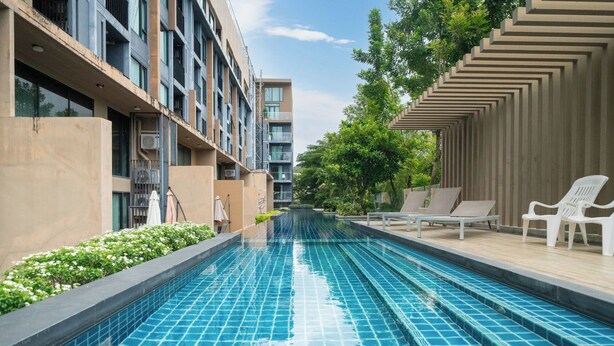 A swimming pool with tiled flooring, surrounded by lounge chairs and a building with multiple balconies. - Best for Digital Nomad-1 BR Apt close to Surin Beach (Tambon Choeng Thale)